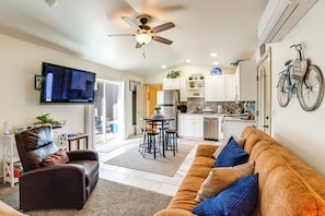 A modern living room with a sofa, a television, a ceiling fan, and a kitchen area with white cabinets and a bicycle mounted on the wall. - 4 Mi to Dtwn! Grand Junction Stay w/ Private Pool (Grand Junction)