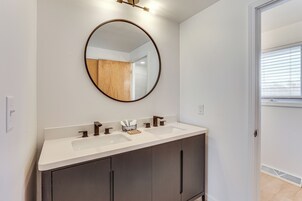 Un baño con tocador blanco, espejo redondo y ventana con persianas.