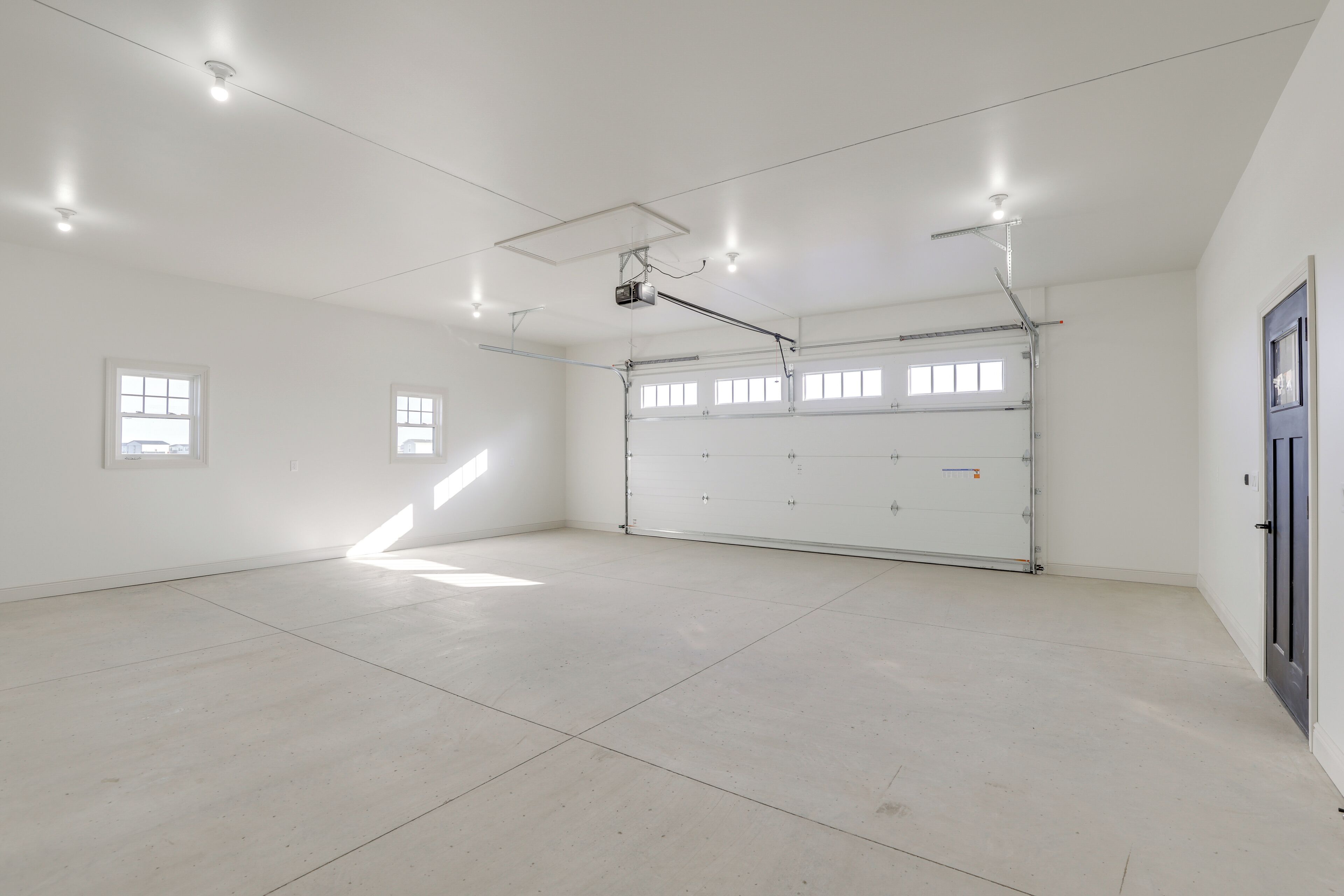 A spacious, well-lit garage with a large door, ceiling lights, and windows.