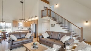 Amplia sala de estar con dos sofás de cuero, una mesa de centro de madera y una escalera que conduce a un nivel superior.