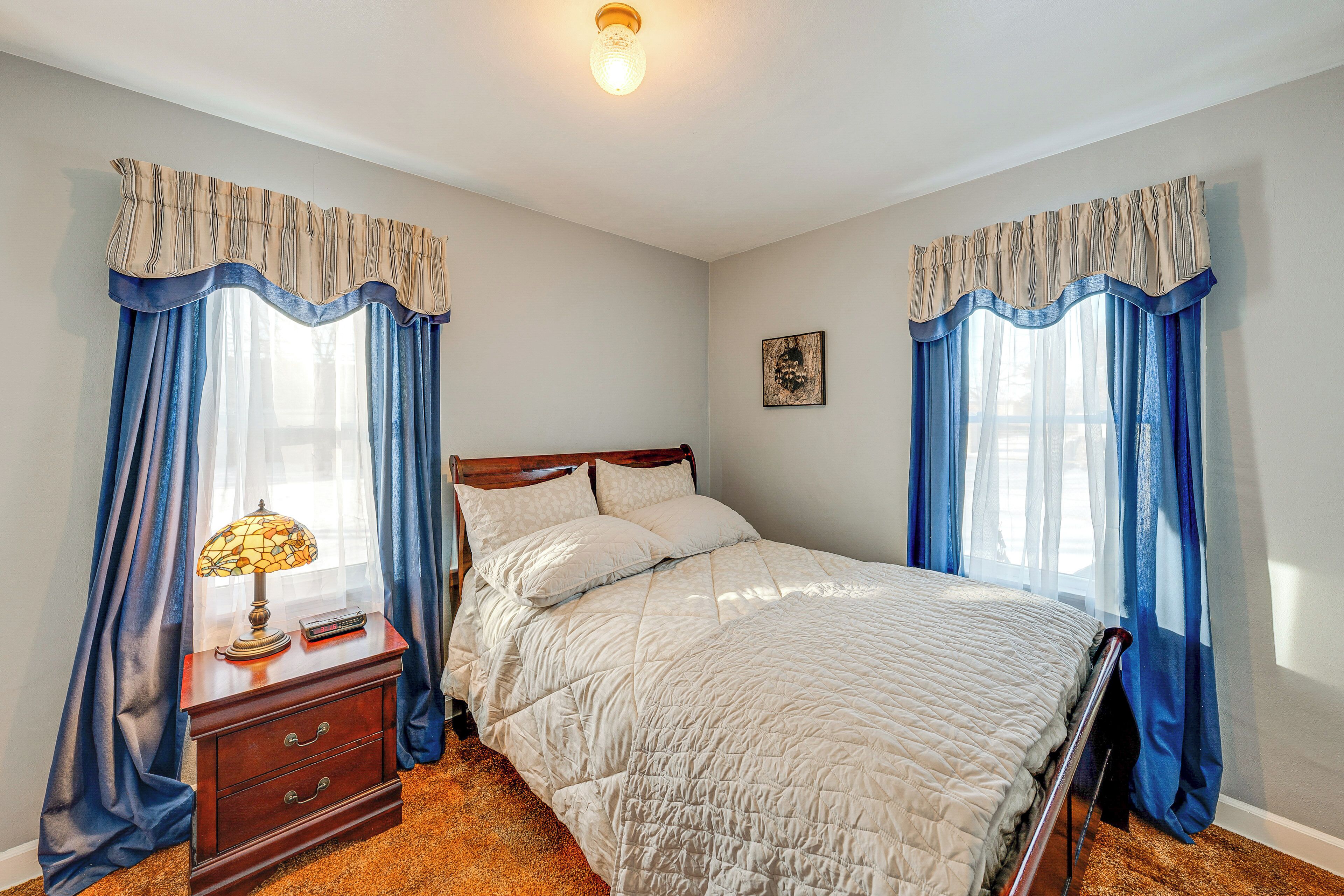 A bedroom with a bed, a nightstand, a lamp, and curtains.