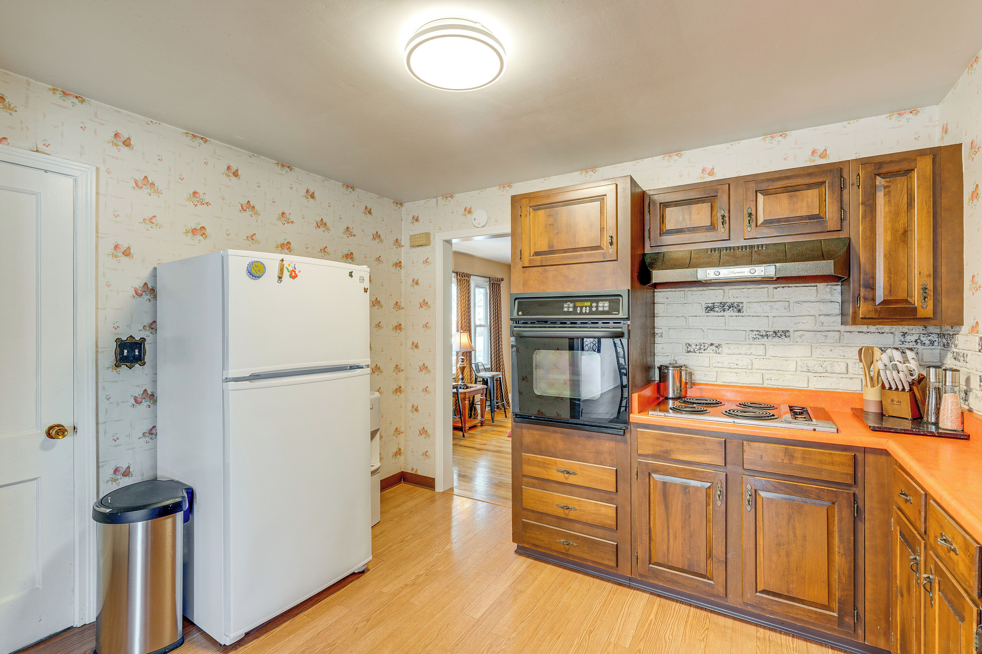 A kitchen with wooden cabinets, a white refrigerator, a stove, and a trash can.