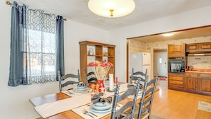 Zona pranzo con tavolo in legno apparecchiato per quattro persone, un lampadario e vista sulla cucina.