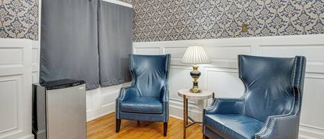 A room with two blue leather chairs, a small table with a lamp, and a refrigerator.