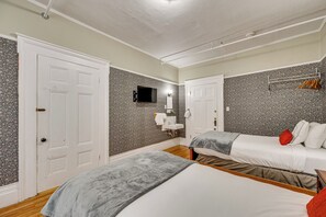 A bedroom with two beds, a white door, a mounted TV, a small bathroom with a sink, and a coat rack. - On Historic Main Street: Walkable & Quaint Apt! (Littleton)
