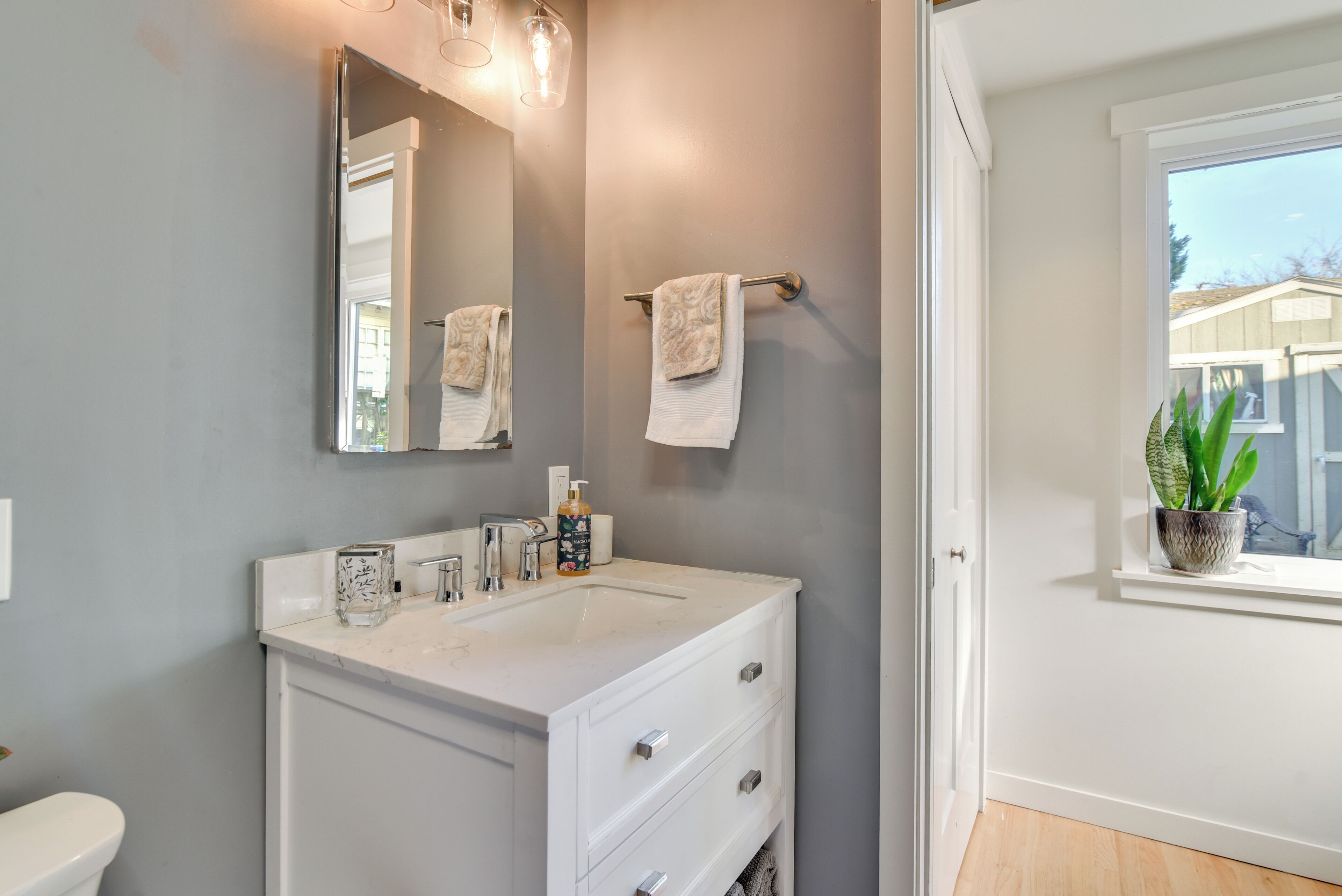 A bathroom with a white vanity, a large mirror, and a potted plant by the window.