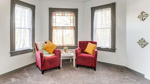 Une pièce d’angle avec deux fauteuils rouges, une petite table et une fenêtre ornée de rideaux à motifs.