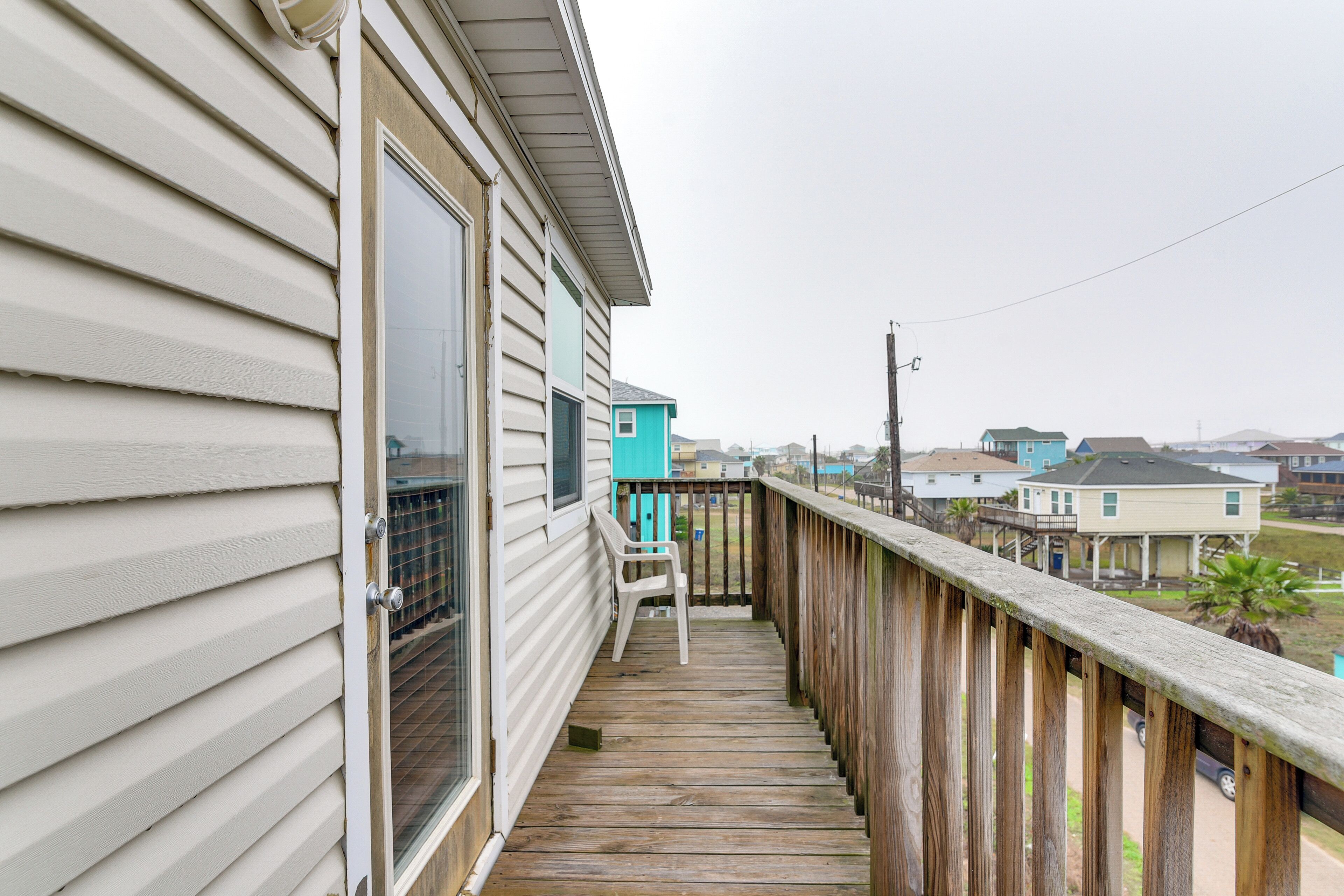 A wooden deck with a chair, a window, and a view of neighboring houses.