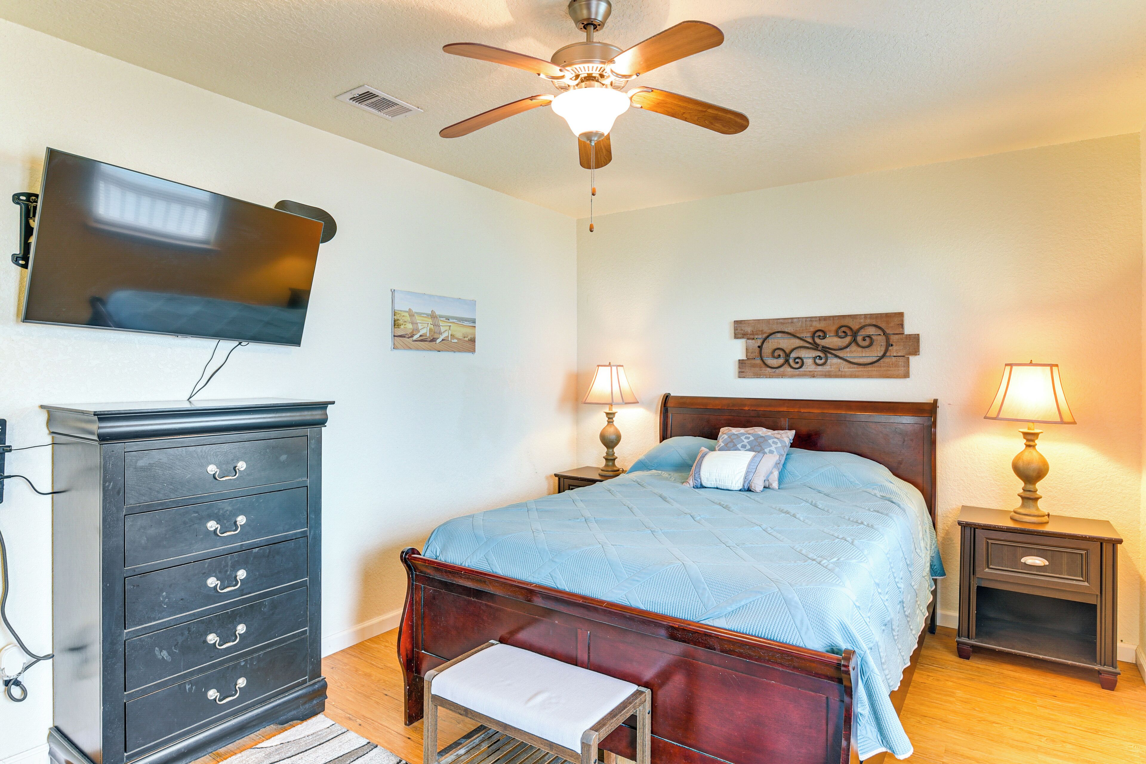 A bedroom with a bed, nightstands, a dresser, a ceiling fan, and a television mounted on the wall.