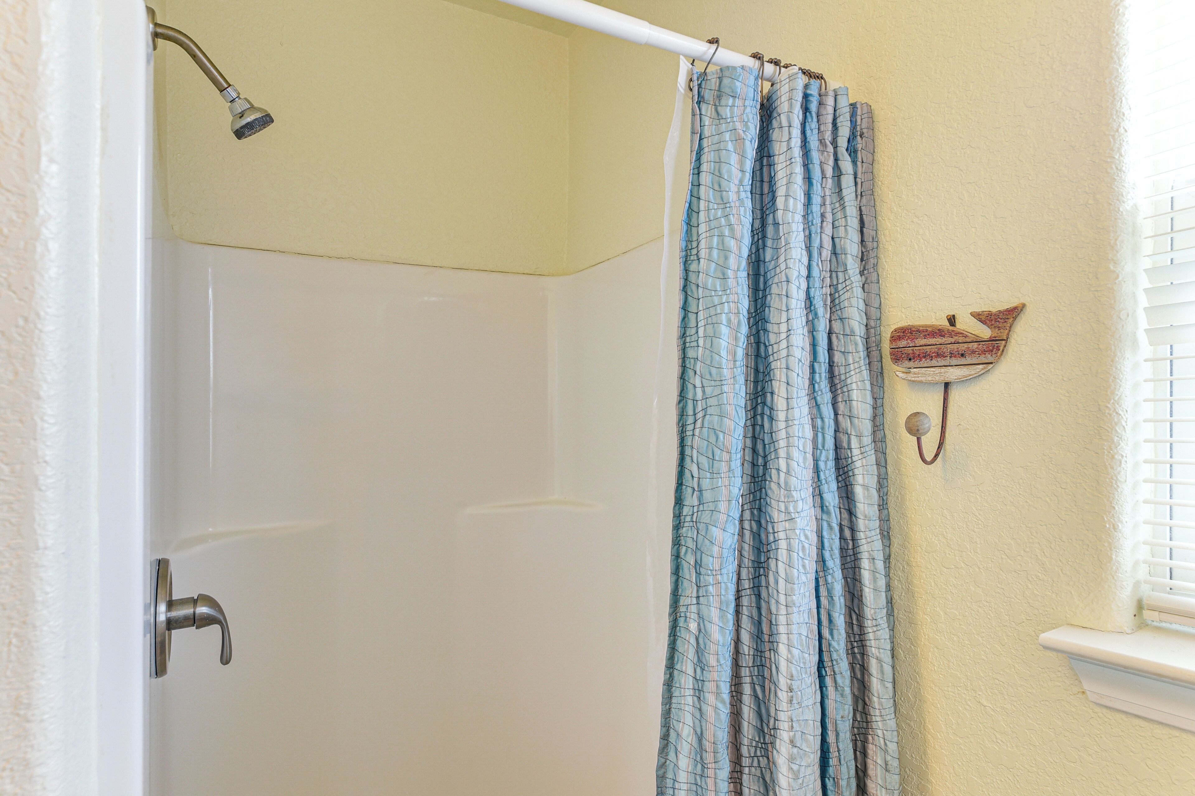 Un baño con cortina de ducha, grifo de pared y ventana con persianas.