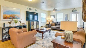 A living room with a sofa, coffee table, and a TV. There are decorative items on shelves and a ceiling fan. - Daves Waves Pet-friendly Home in Surfside Beach (Freeport)