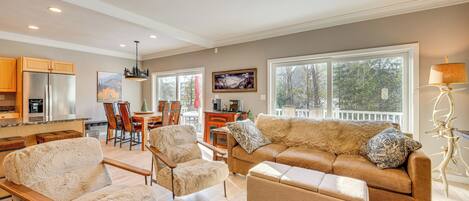 A spacious living area with a large sofa, two armchairs, and a coffee table. There is a dining area with a table and chairs, and a kitchen with a refrigerator and cabinets.