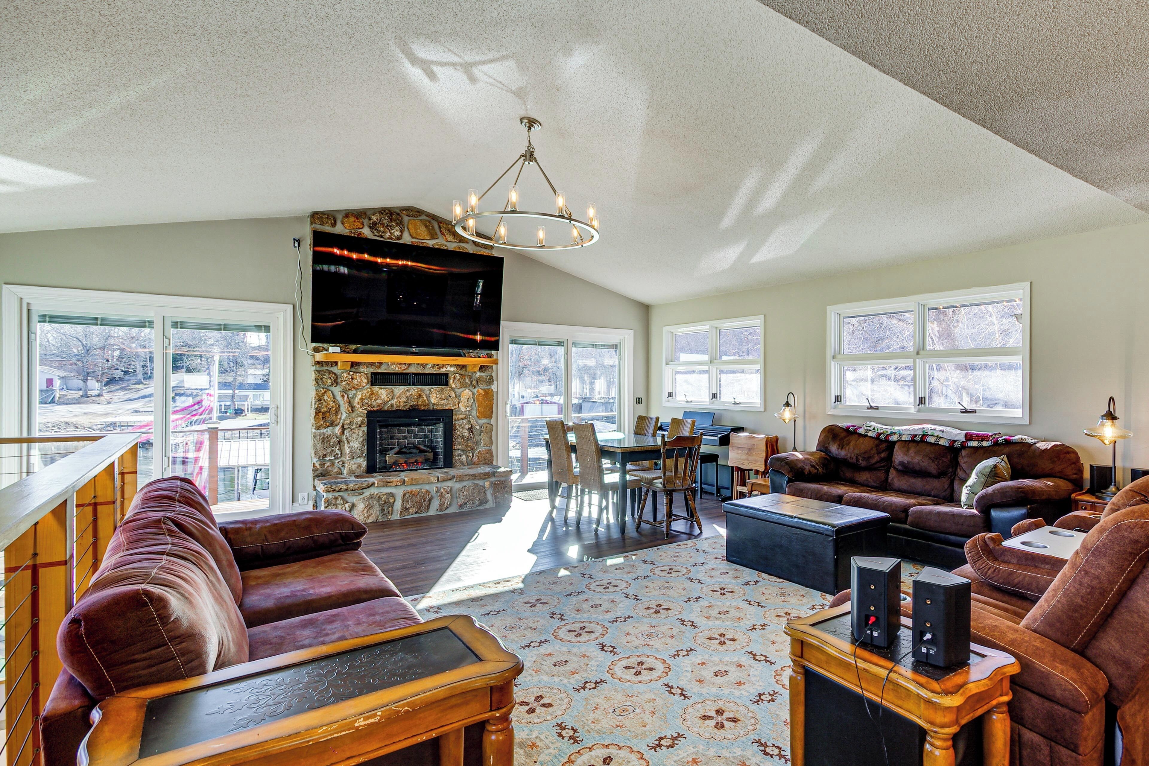A spacious living room with a stone fireplace, leather sofas, a dining area, and large windows.