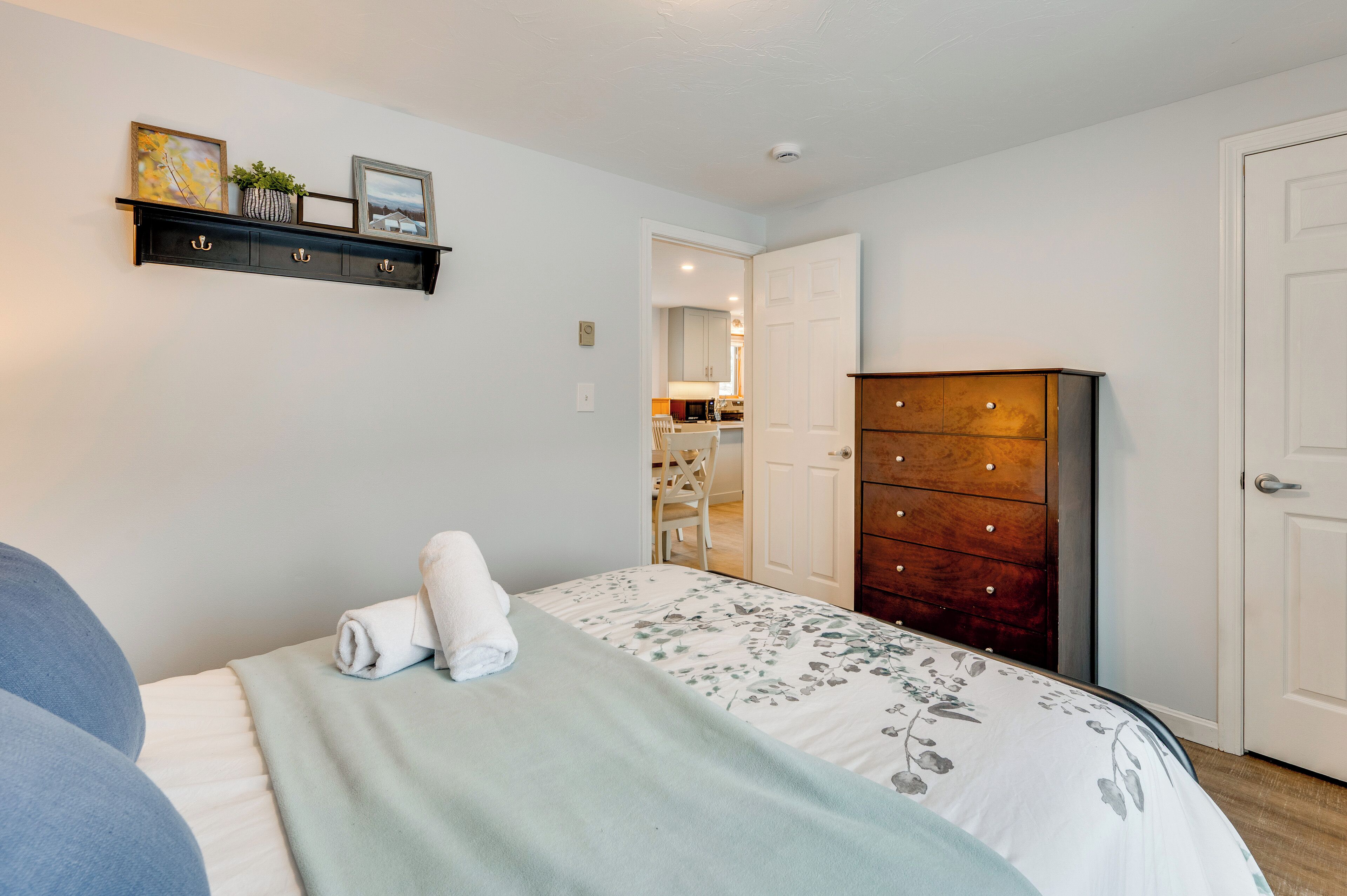 Un dormitorio con una cama, un aparador, una estantería con fotos y una puerta que da al baño.