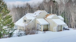 Una casa con techo inclinado, rodeada de árboles y cubierta de nieve.