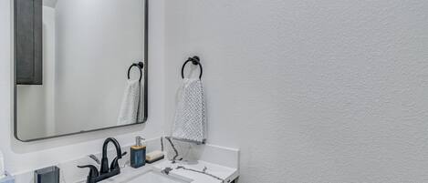 Et badeværelse med et stort spejl, en hvid vask med marmorbordplade og to håndklæder hængende på håndklæderinge.