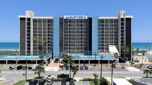 Un hôtel à plusieurs étages, reconnaissable à son grand panneau « SUNTIDE III », un parking avec plusieurs voitures et une vue sur l’océan.