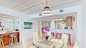 A modern kitchen with white cabinets, a dining area with a glass table, and a kitchen island with stools. - Shorefront 2br, Luxe Perks: Suntide III - Unit 704 (South Padre Island)