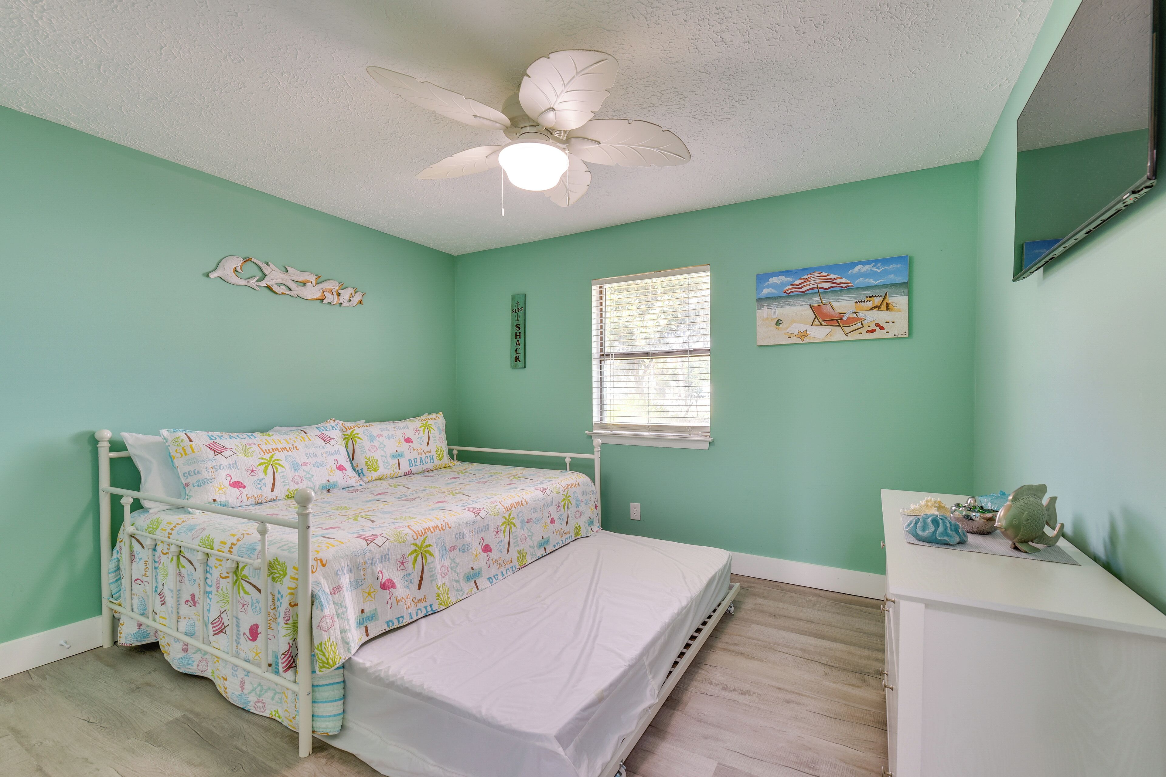 Une chambre à coucher avec un lit, un ventilateur de plafond, une fenêtre et une commode.