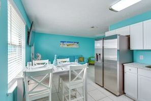 A kitchen with white cabinets, a stainless steel refrigerator, and a dining area with white chairs and a table set for two. - Walk to Beach & Rick Seltzer Park! PCB Getaway (Panama City Beach)