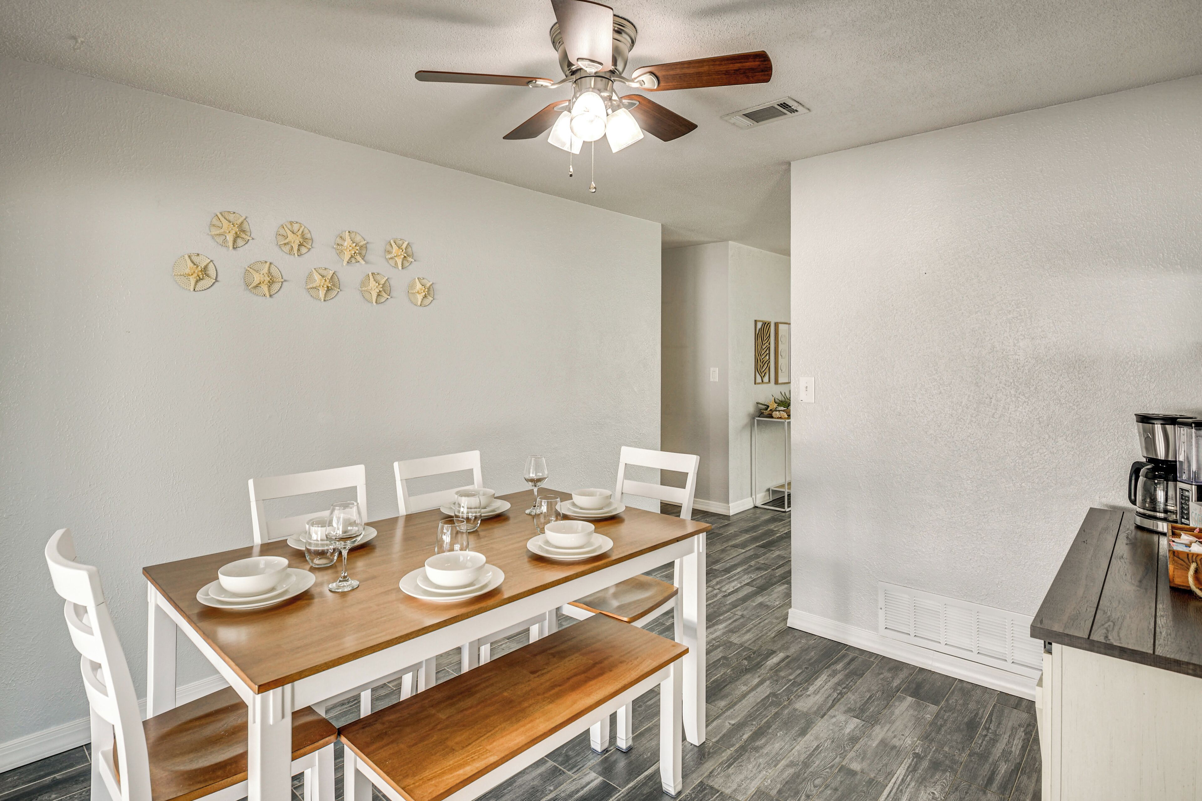 A dining area with a wooden table set for four, white chairs, and a ceiling fan.