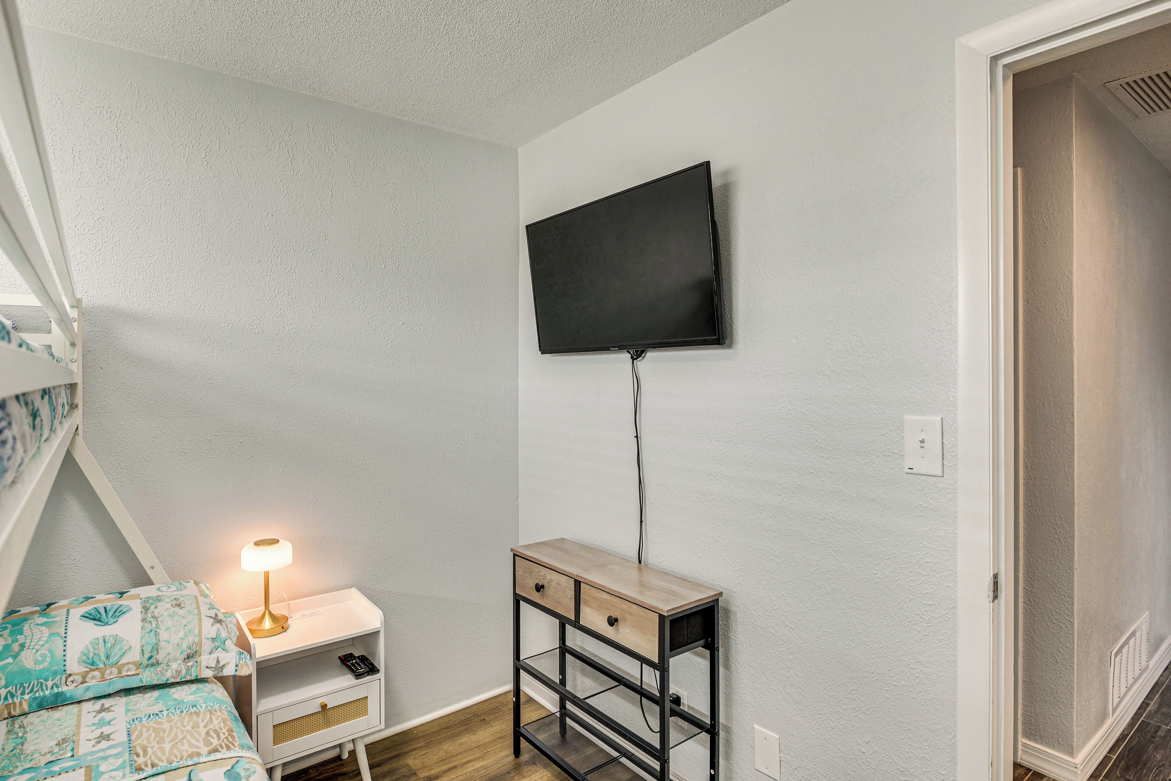 A bedroom with a bed, a bedside table with a lamp, a TV mounted on the wall, and a small wooden cabinet.