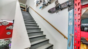 A staircase with a wooden handrail, a red and blue metal structure, and a wall-mounted snowboard rack. - Sportsman's Paradise! St Maries Stay Near Hunting (St. Maries)