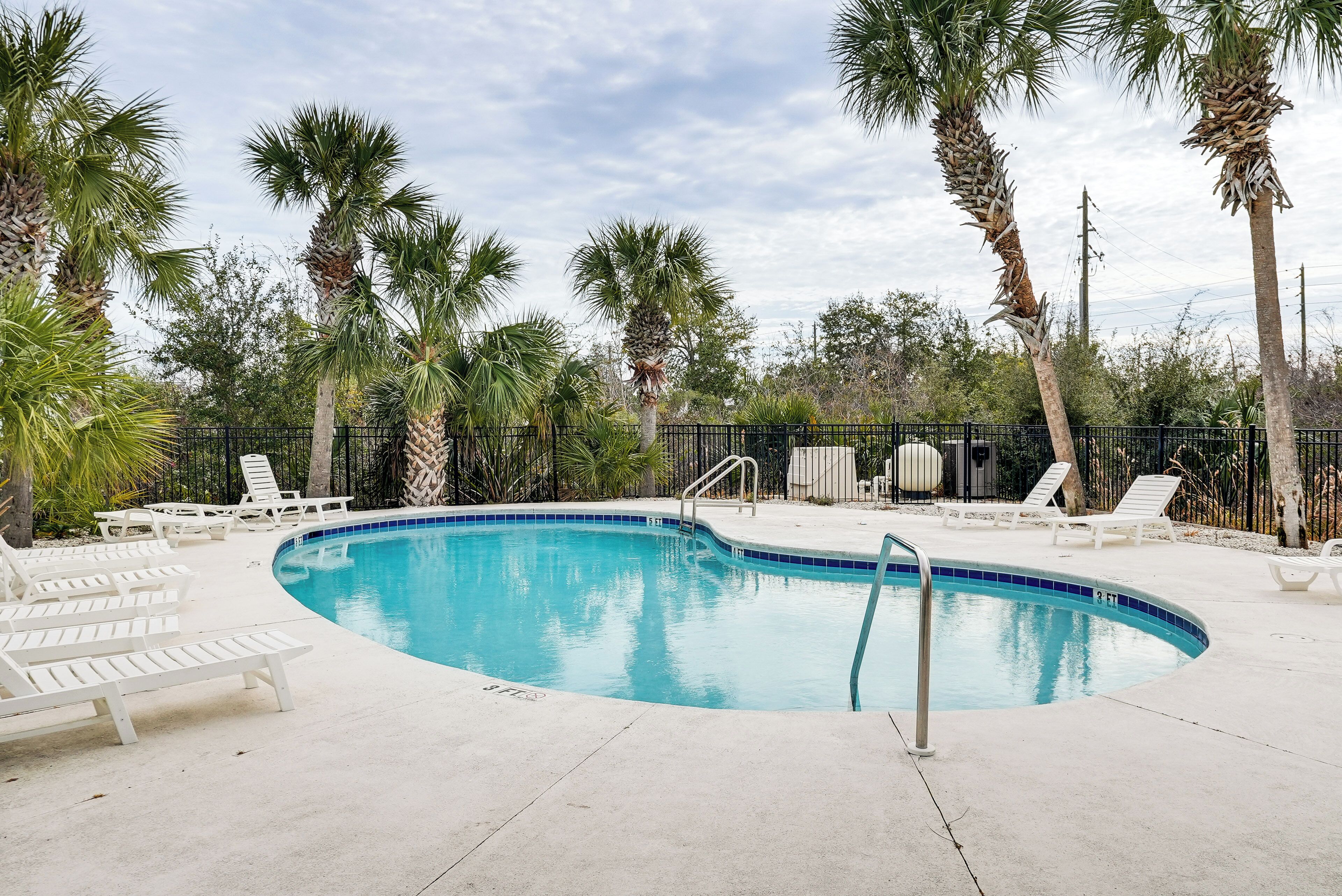 A swimming pool with white lounge chairs and palm trees.