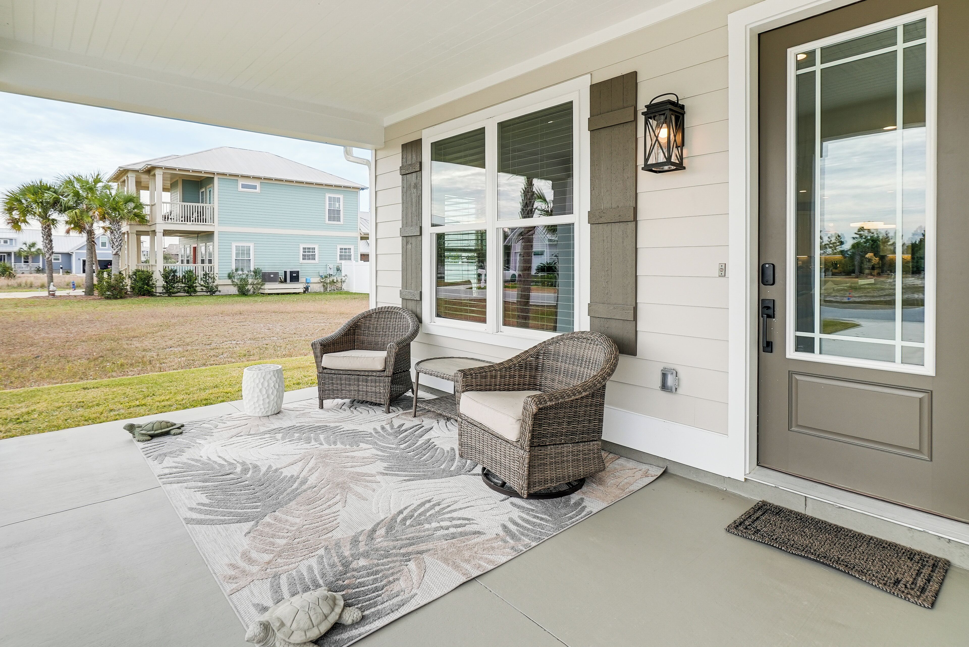 A covered porch with wicker chairs and a large leaf-patterned rug.