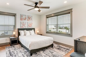 A bedroom with a bed, two bedside tables, a ceiling fan, artwork on the wall, and large windows. - Walk to Beach! 'ocean's Paradise' w/ Patio (Port St. Joe)