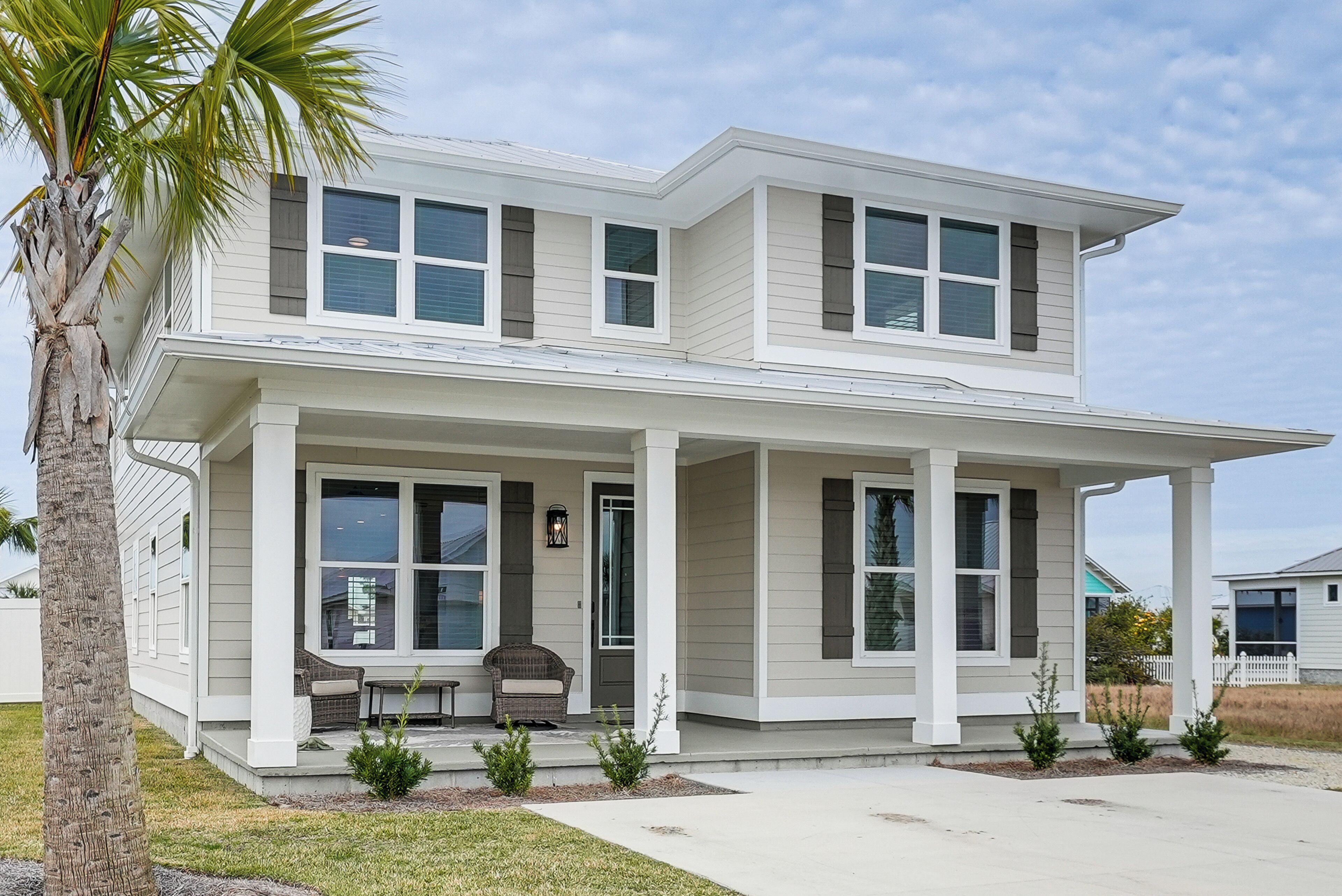 A two-story house with a covered porch, large windows, and a small outdoor seating area.