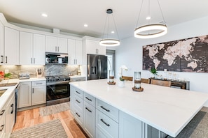 A modern kitchen with white cabinets, stainless steel appliances, a large island, and a world map on the wall. - Walk to Beach! 'ocean's Paradise' w/ Patio (Port St. Joe)