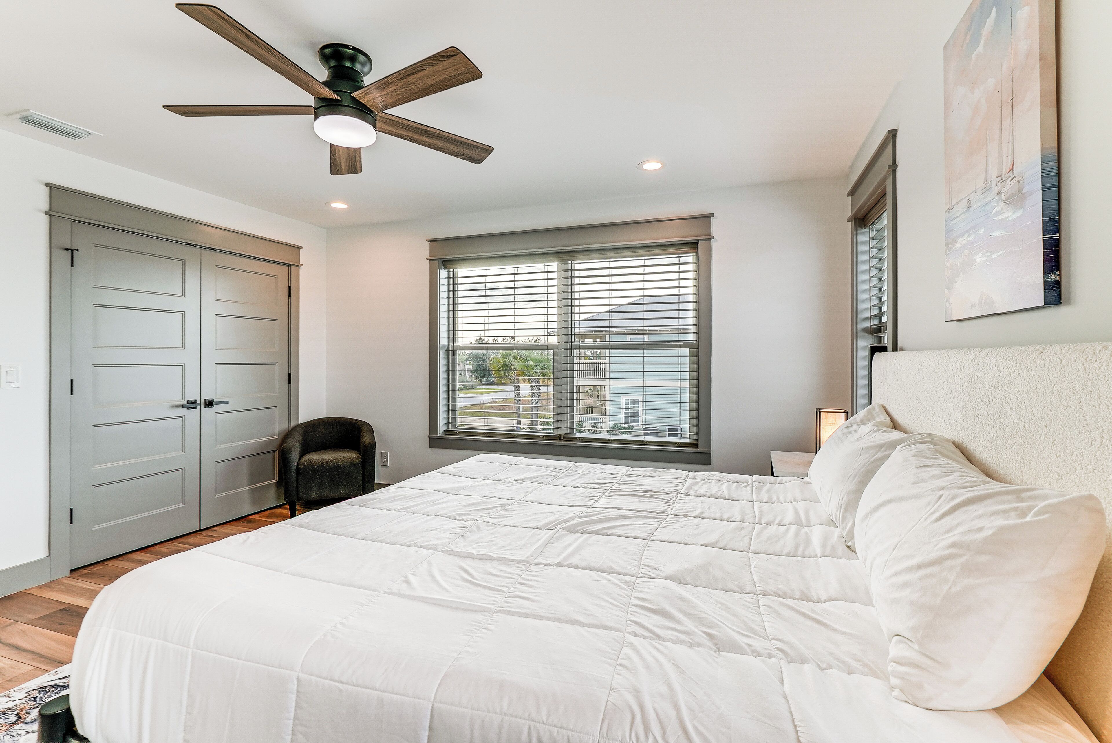 Une chambre avec un grand lit, un ventilateur de plafond, une fenêtre avec des stores et une porte.