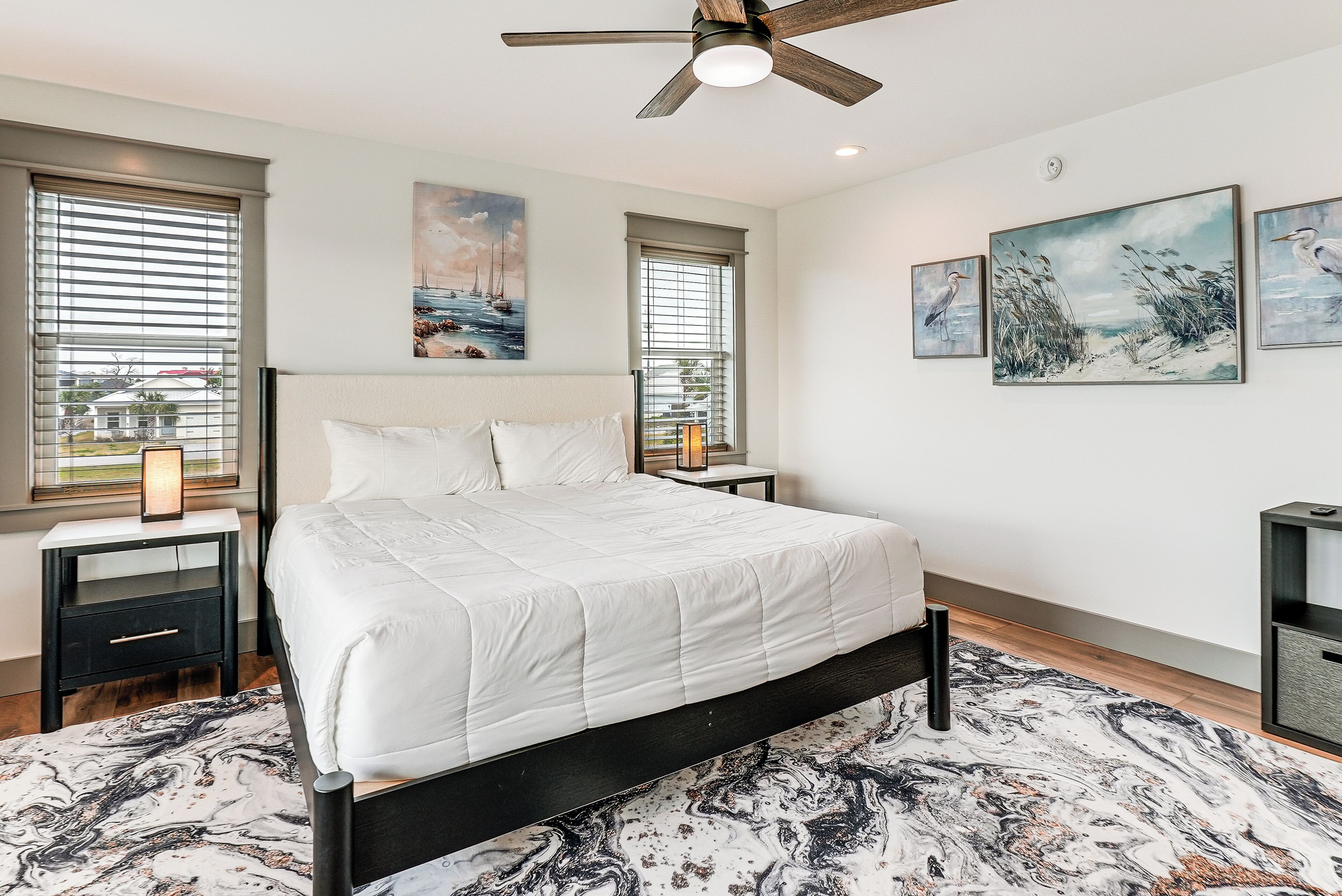 A bedroom with a bed, two nightstands, a ceiling fan, and three wall-mounted paintings.