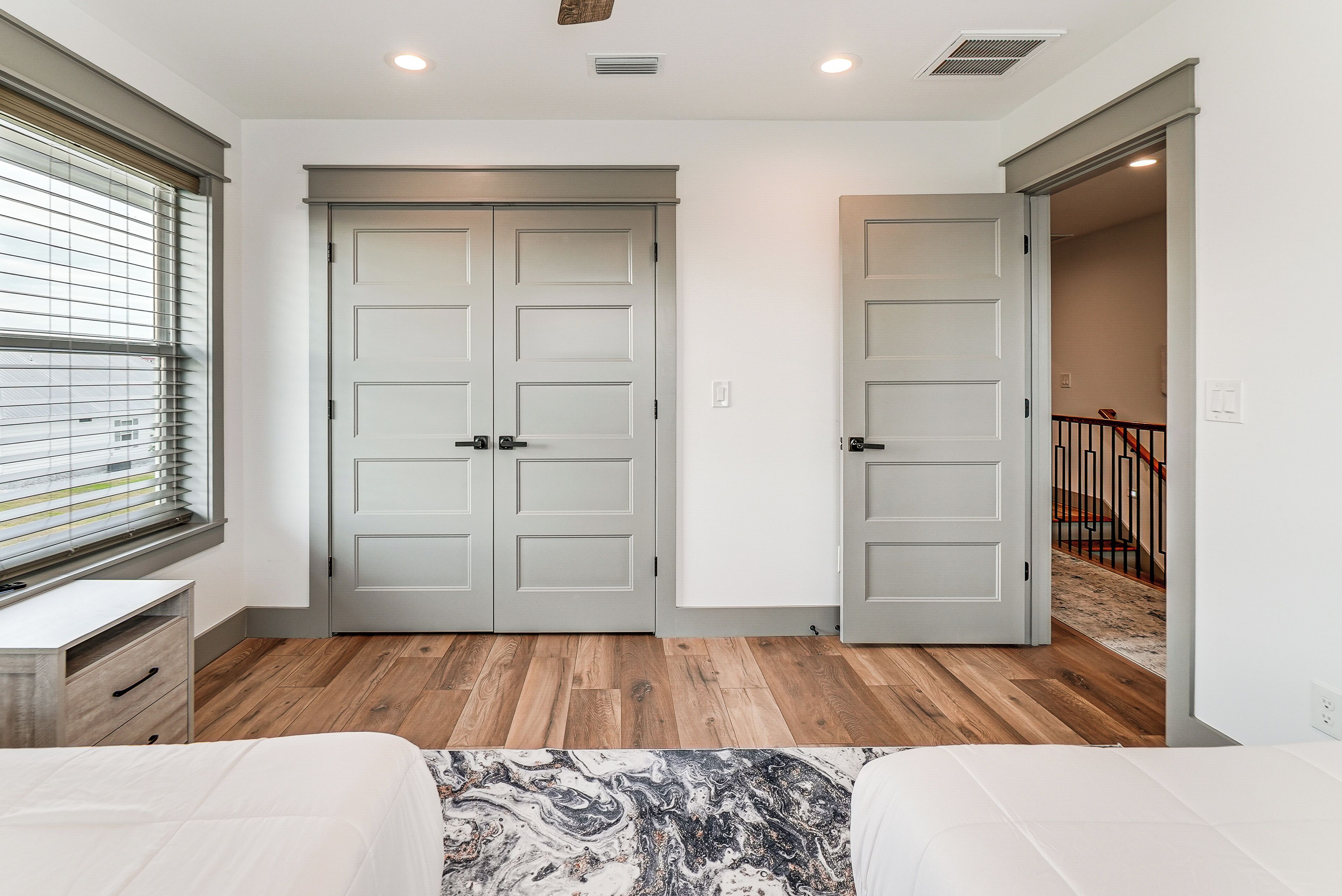 Une chambre avec un plancher en bois, un lit recouvert d’une couvre-lit à motifs et une fenêtre avec des stores.