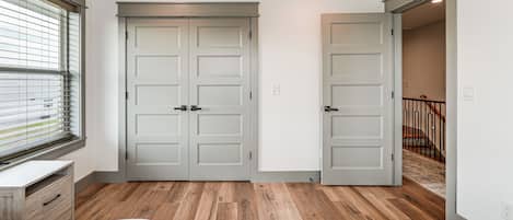Une chambre avec un plancher en bois, un lit recouvert d’une couvre-lit à motifs et une fenêtre avec des stores.