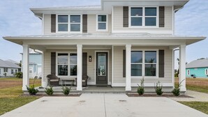 A two-story house with a covered porch, a front door, and a small seating area with a chair and table. - Walk to Beach! 'ocean's Paradise' w/ Patio (Port St. Joe)