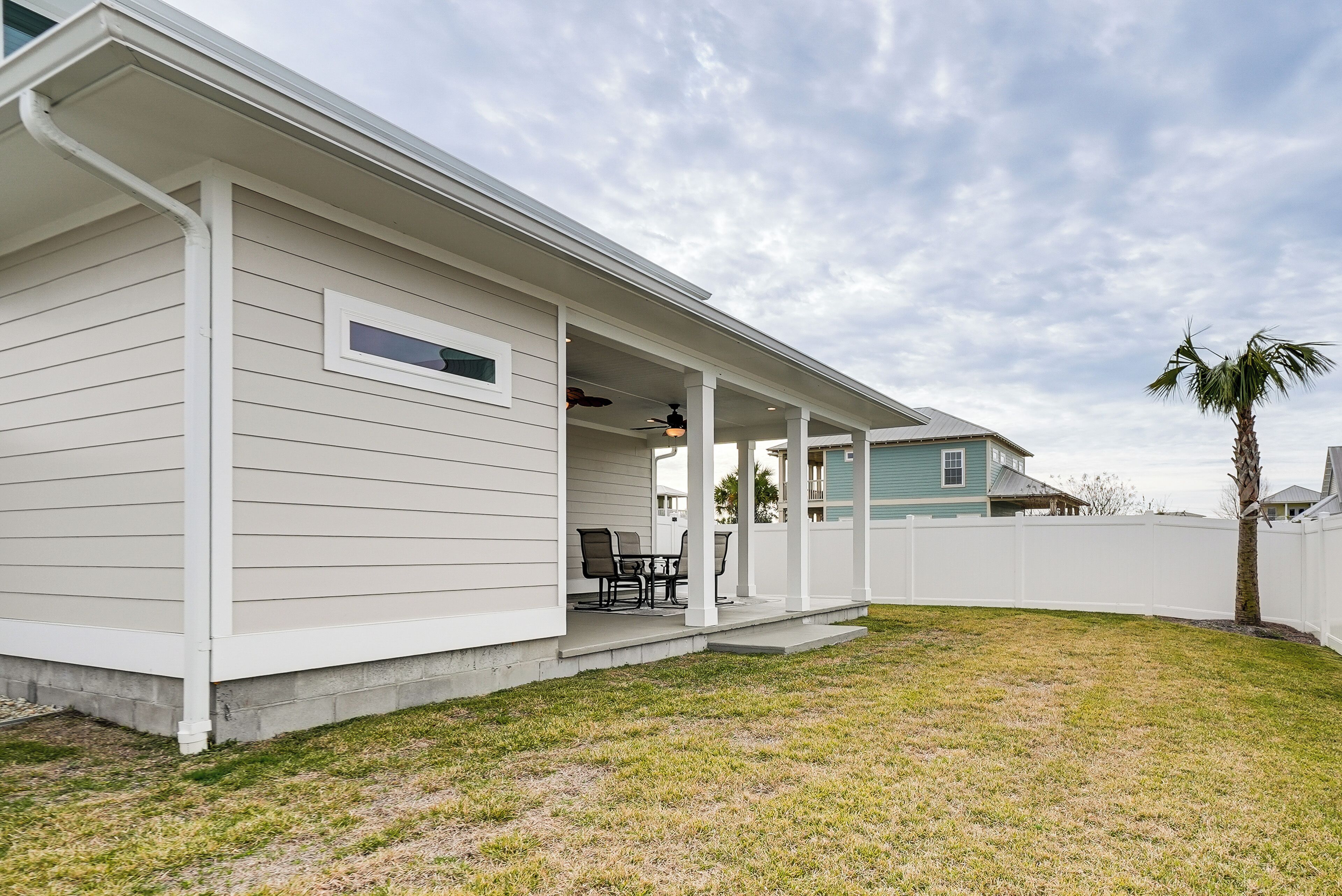 A single-story house with a covered porch, a small patio with a table and chairs, and a white fence surrounding the property.