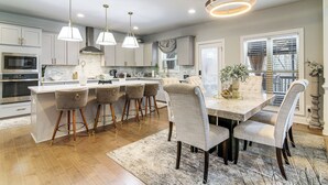 A modern kitchen with a central island, bar stools, pendant lighting, and a dining area with chairs. - 9 Mi to Mystic Falls Tours! Spacious Group Getaway (Covington)
