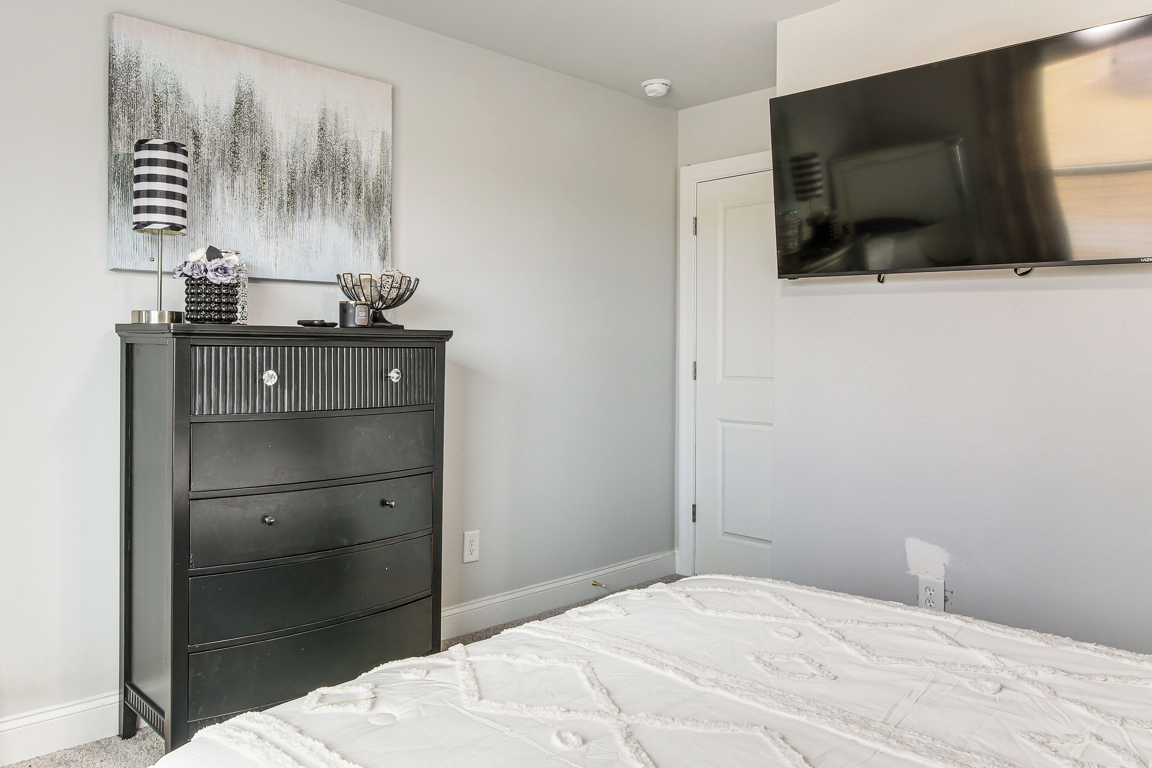 A bedroom with a bed, dresser, and a mounted TV.