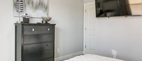A bedroom with a bed, dresser, and a mounted TV.