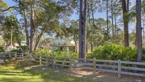 A wooden fence, a house with a green roof, and tall trees in a wooded area. - 1/2 Mi to Beach! Rural Home w/ Deck in Port St Joe (Port St. Joe)