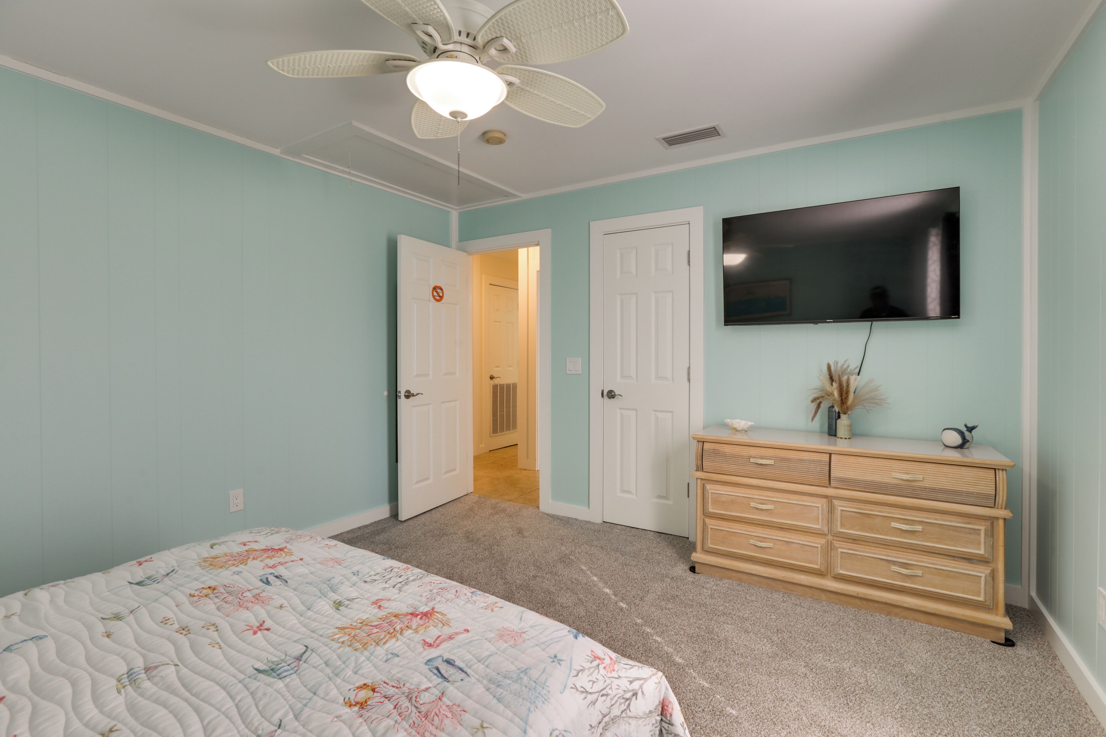 A bedroom with a bed, a dresser, a ceiling fan, and a TV on the wall.