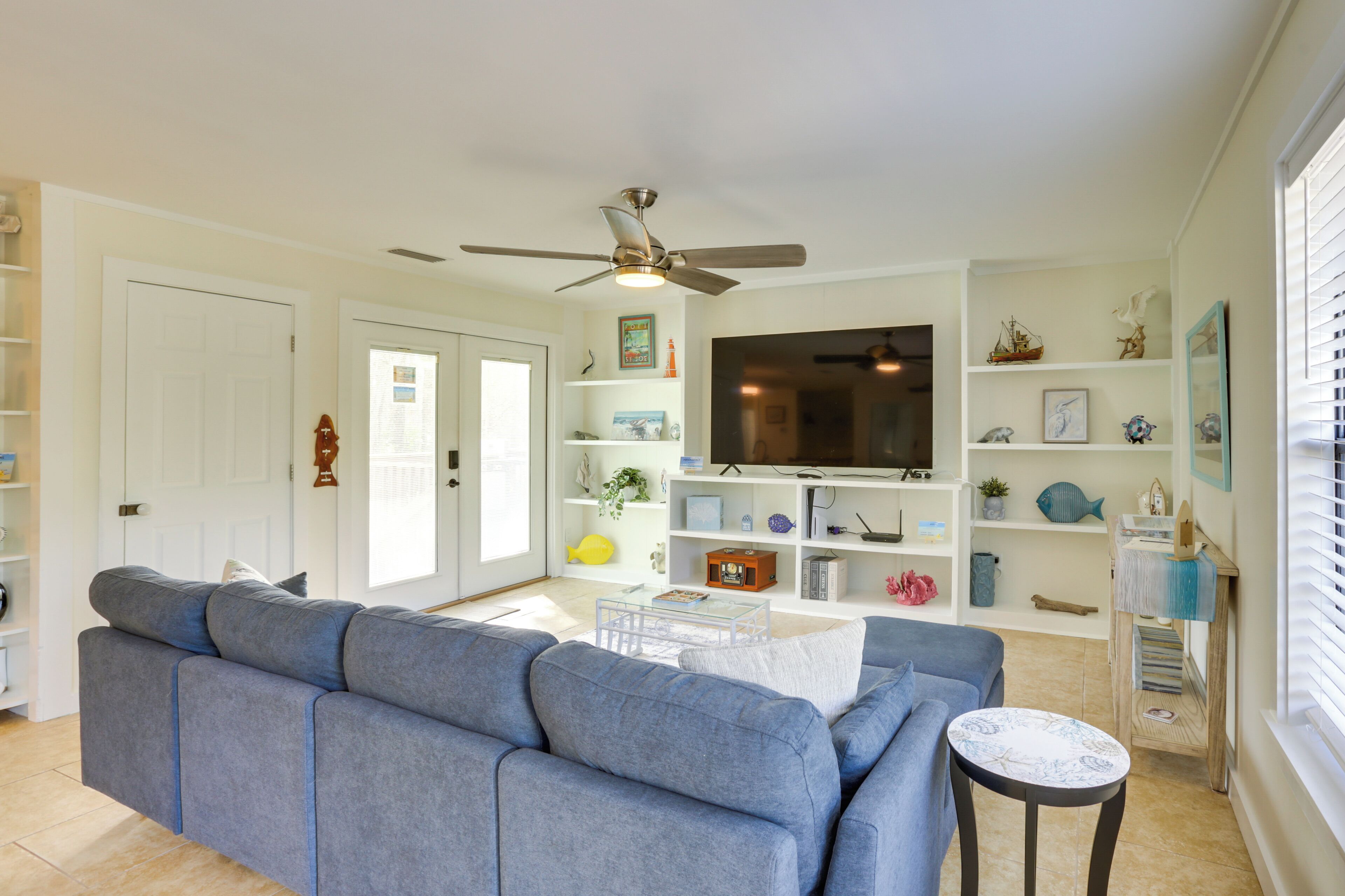 A living room with a grey sofa, a TV, and shelves with decorative items.