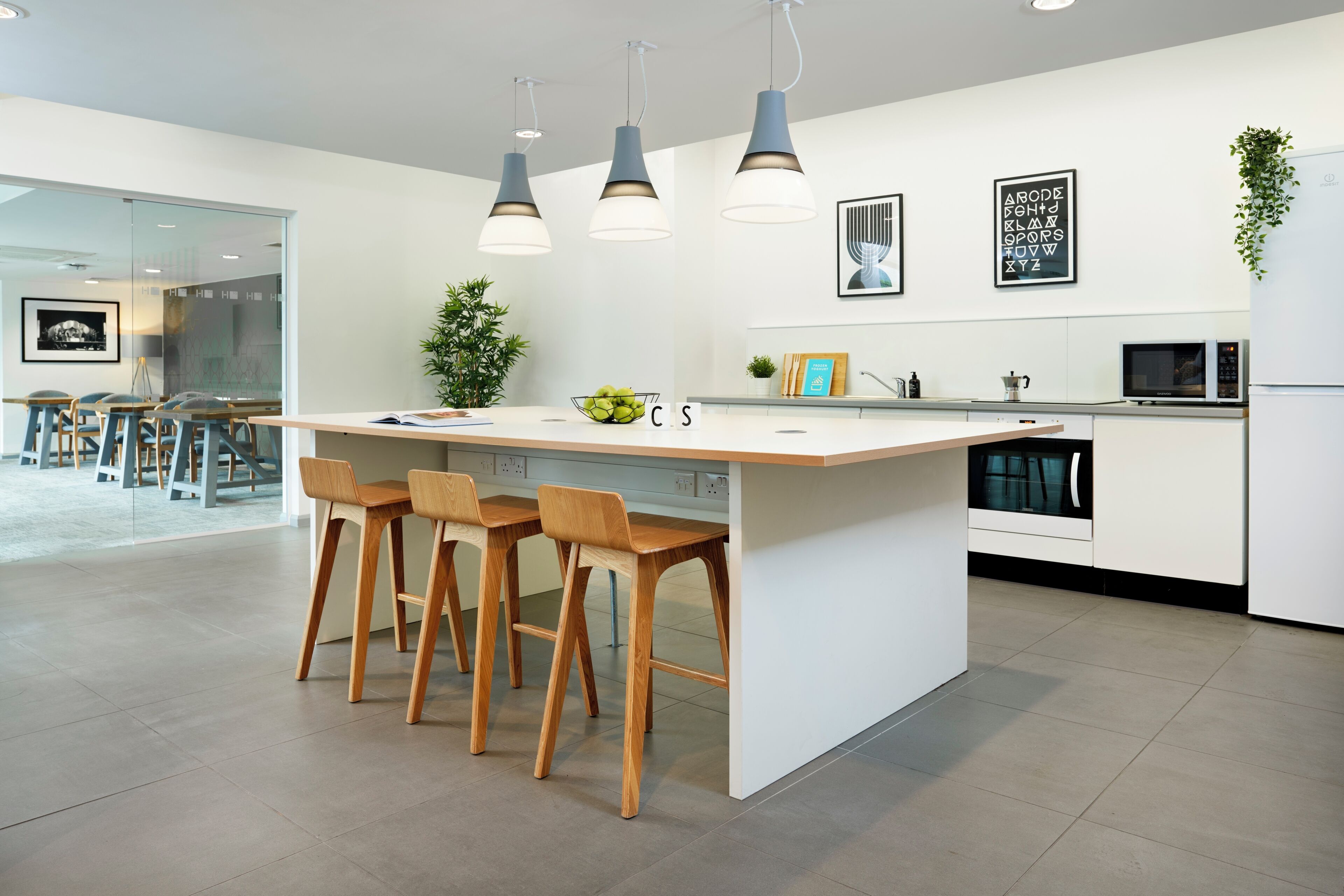 A modern kitchen with a central island, bar stools, pendant lighting, and a microwave.