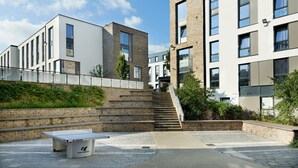 A modern building with a staircase leading to a second floor, a flat roof, and a paved outdoor area with a table. - For Students Only Ensuites in Southampton (Southampton)