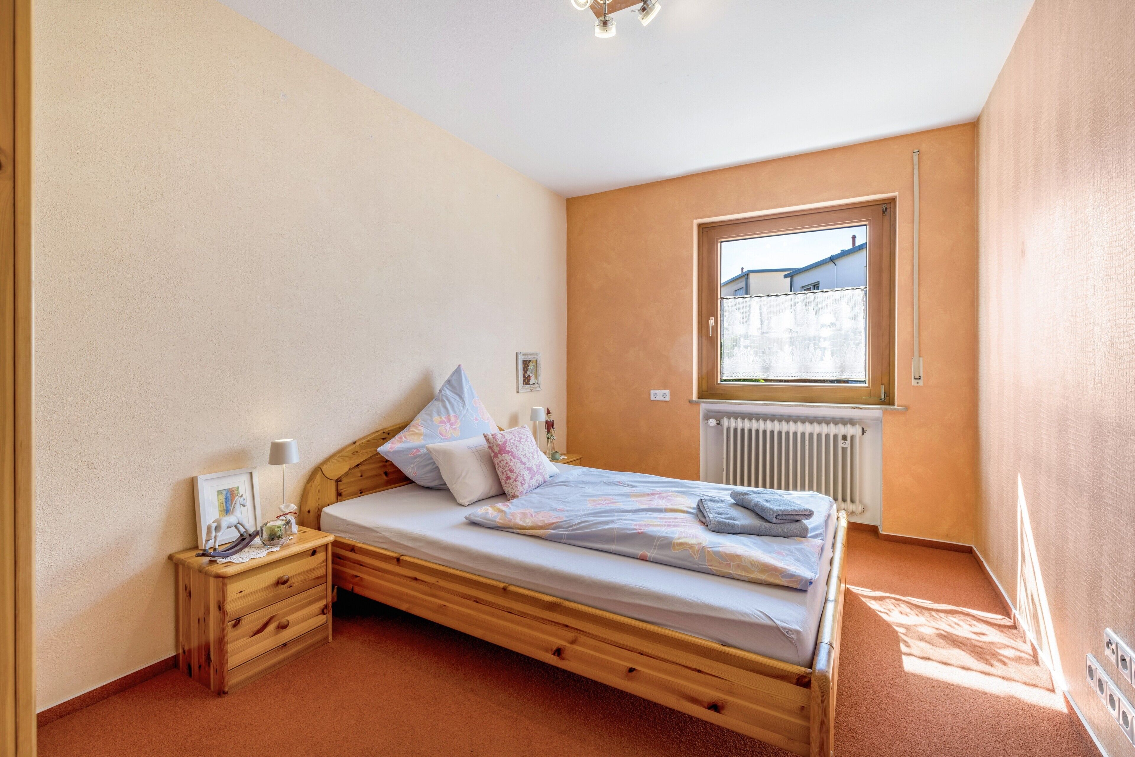 A bedroom with a wooden bed, a nightstand, a window, and a radiator.