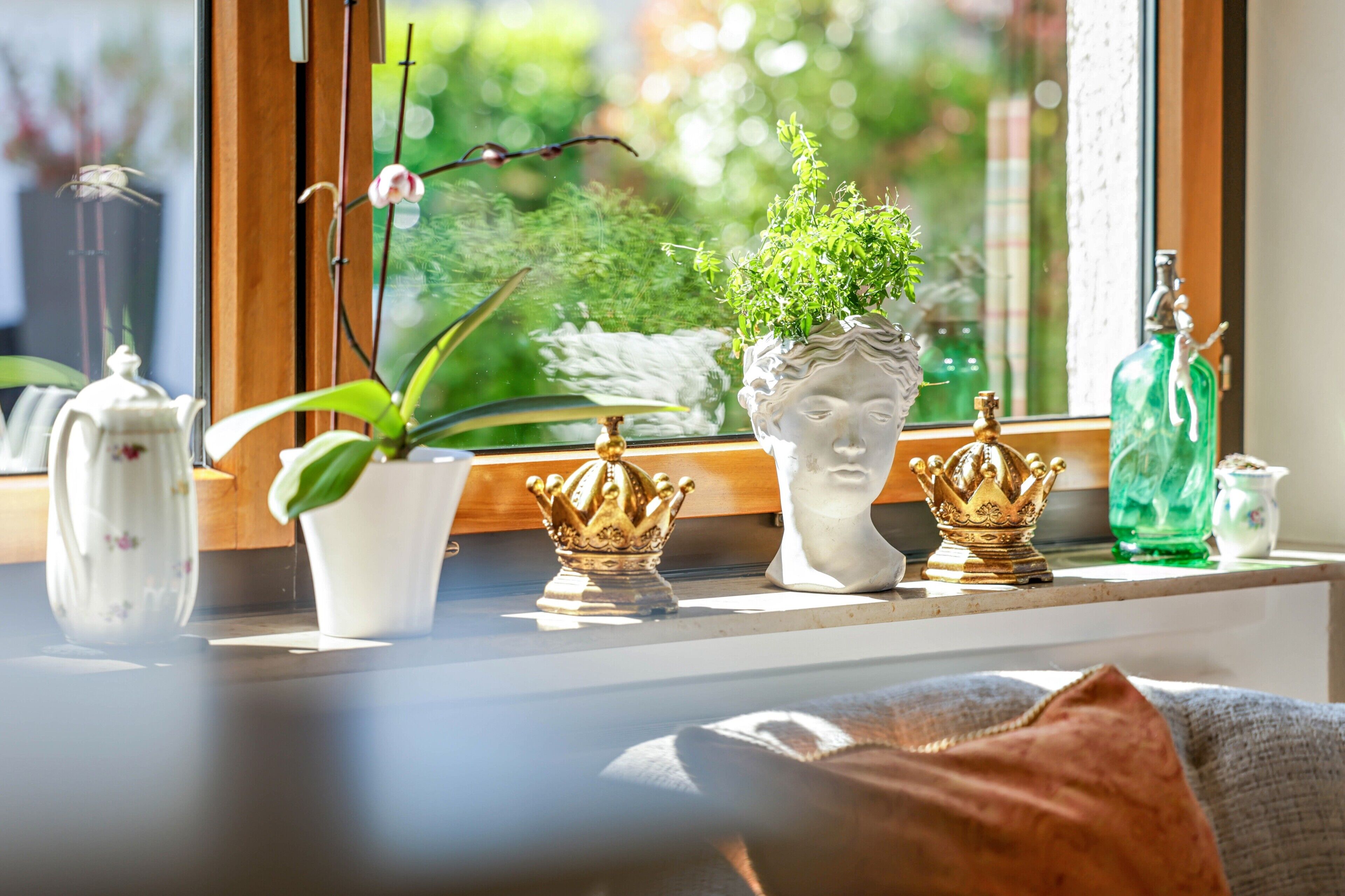 A window sill with a potted plant, a decorative bust, and two golden crowns.
