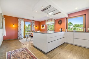 Eine moderne Küche mit einer zentralen Kochinsel, großen Fenstern und Blick ins Grüne.