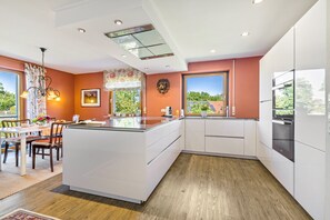 Una cocina moderna con una isla central, muebles blancos y un amplio ventanal con vistas a la vegetación.